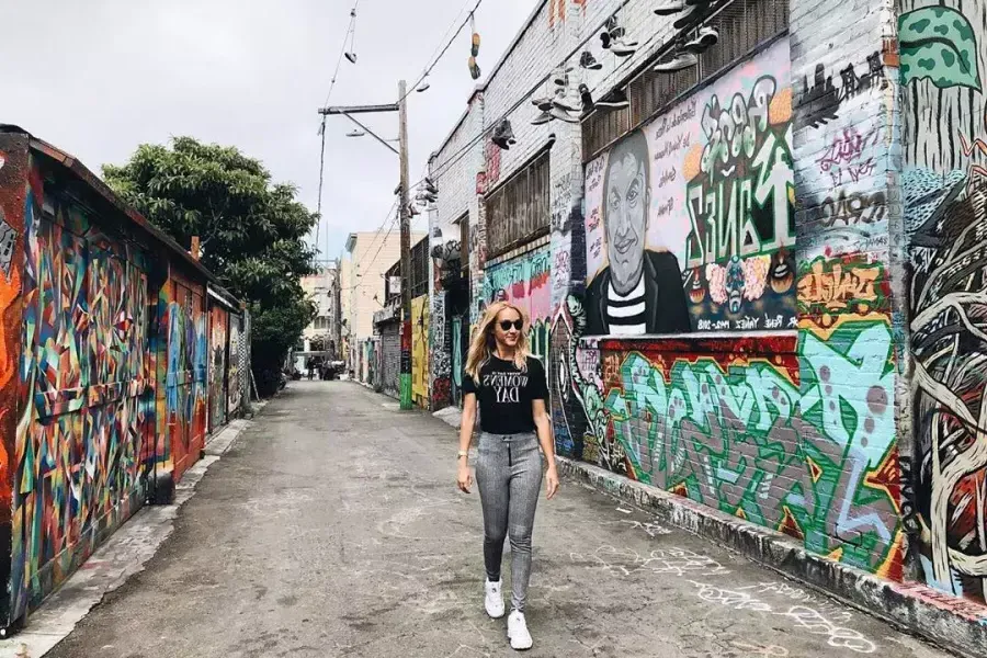 A woman walks through an alley in 教会区 that is covered with murals 和 artwork. 贝博体彩app，加利福尼亚.