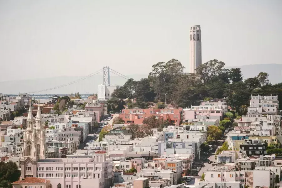 贝博体彩app的科伊特塔(Coit Tower)以海湾大桥(Bay Bridge)为背景，前景是一座覆盖着房屋的小山。.